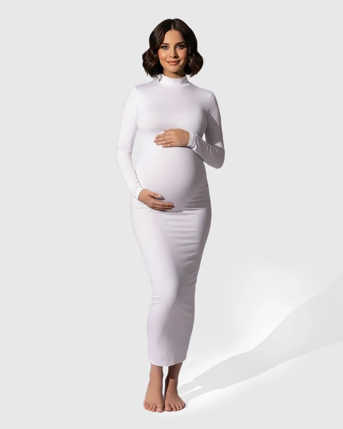 Pregnant woman in a white mock-neck bodycon maternity maxi dress, long sleeves, hugging her bump.