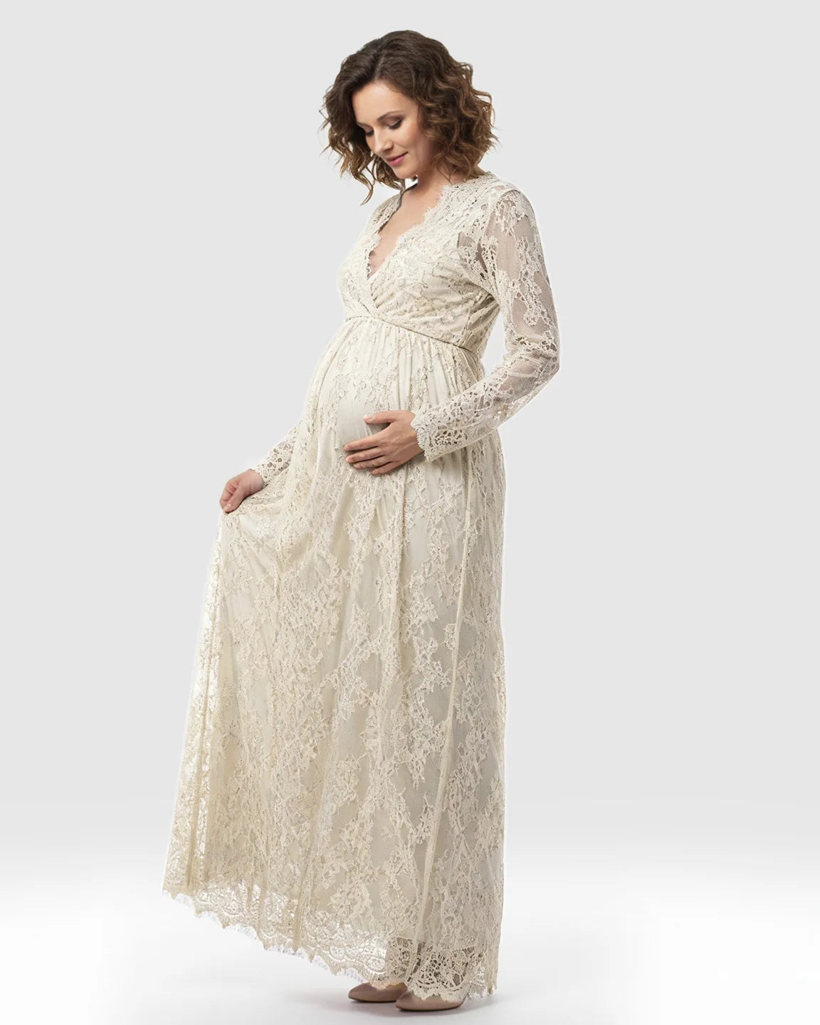 Pregnant woman in a cream sheer floral lace empire waist maternity maxi dress with long sleeves.