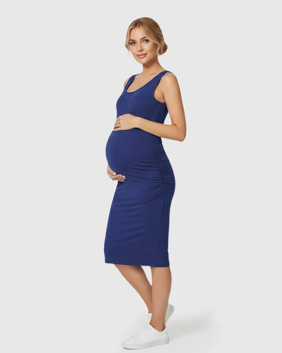 Pregnant woman in a navy blue sleeveless bodycon maternity dress with side ruching, wearing white sneakers.