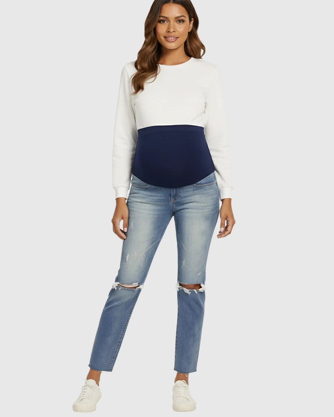 Woman wearing distressed light wash maternity jeans with a navy belly band and white long-sleeve top.