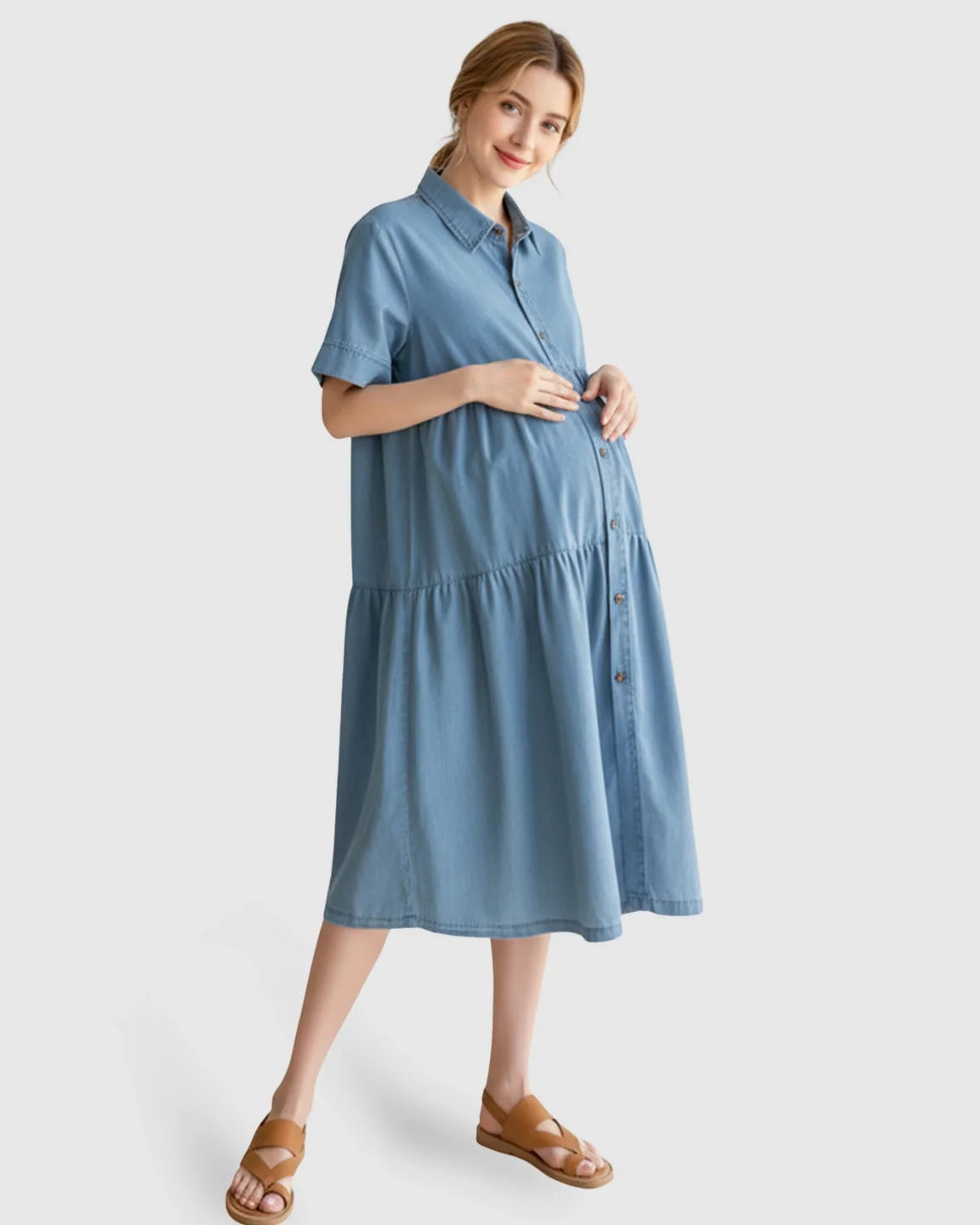 Smiling pregnant woman in a light blue tiered denim maternity midi dress with short sleeves and button front.
