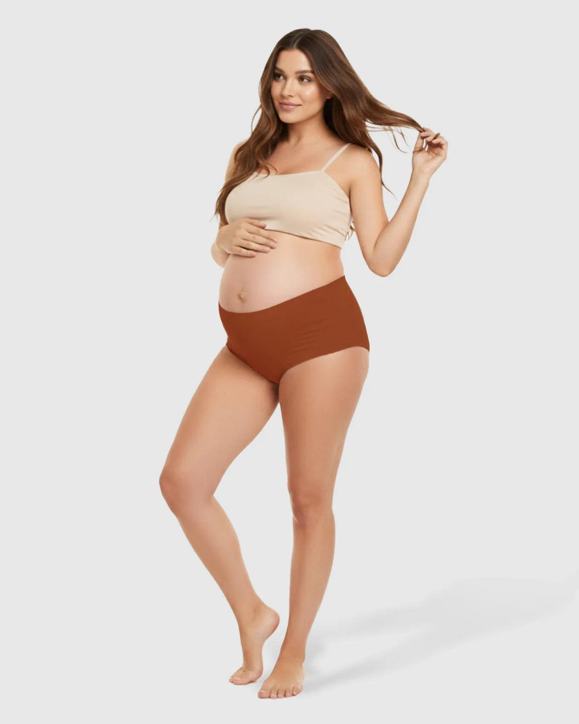 Pregnant woman in a beige bralette and seamless rust-colored high-waist maternity support underwear.