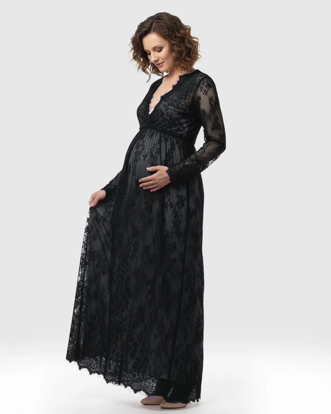 Pregnant woman in a black sheer floral lace empire waist maternity maxi dress, holding her bump.