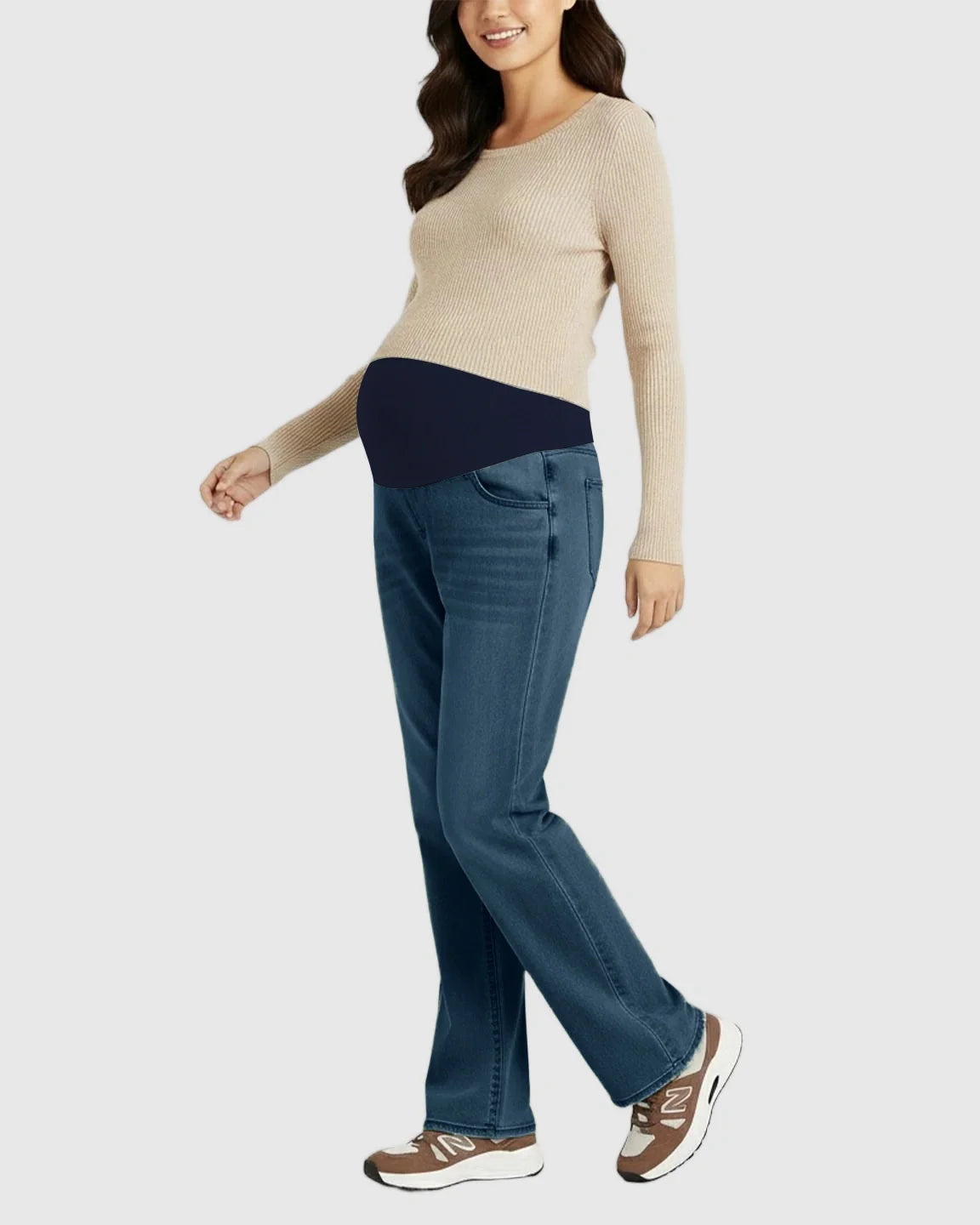 Smiling pregnant woman wearing blue straight-leg maternity jeans with a navy belly band and a beige sweater.