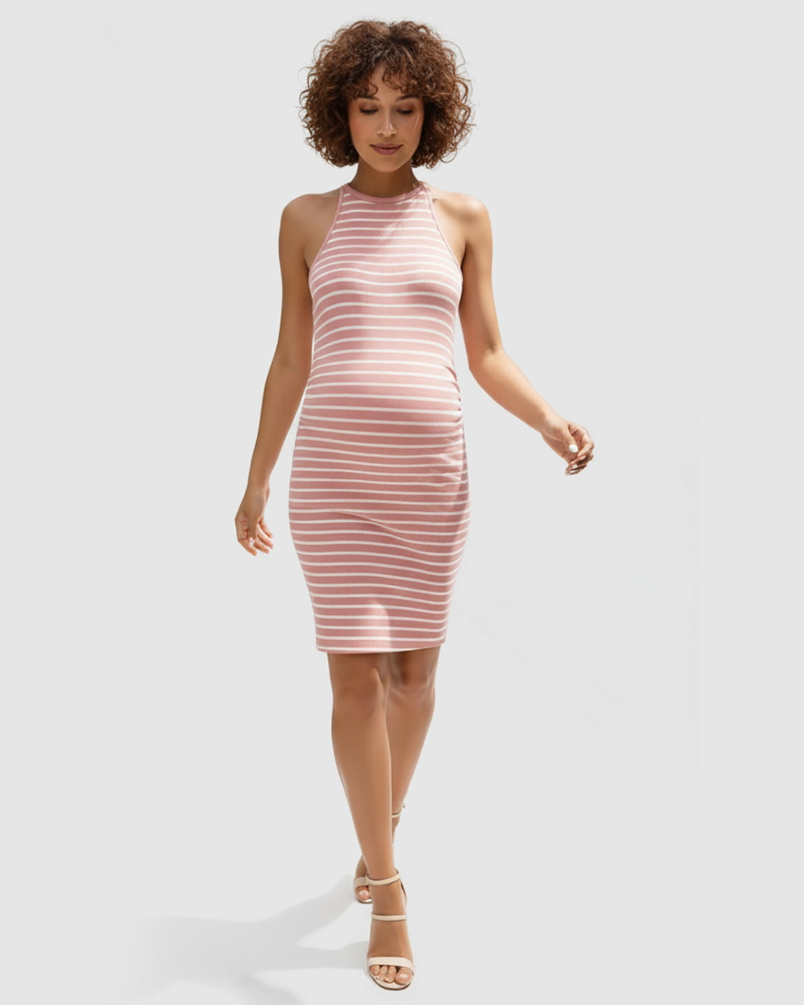 Woman in a pink and white striped halter bodycon maternity mini dress, with a visible baby bump.