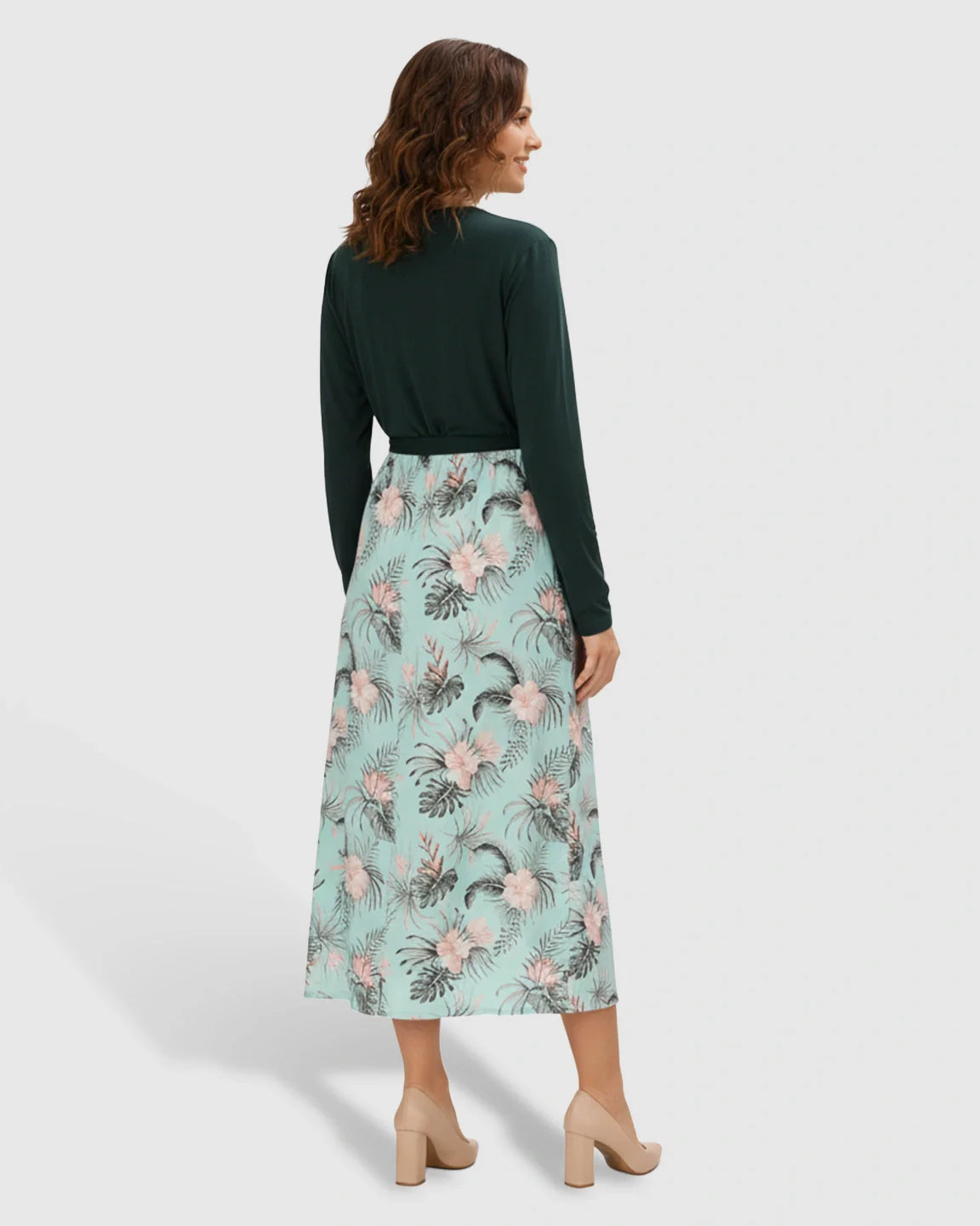 Woman in a deep green long-sleeve v-neck maternity midi dress with a flowing floral skirt and tie waist.