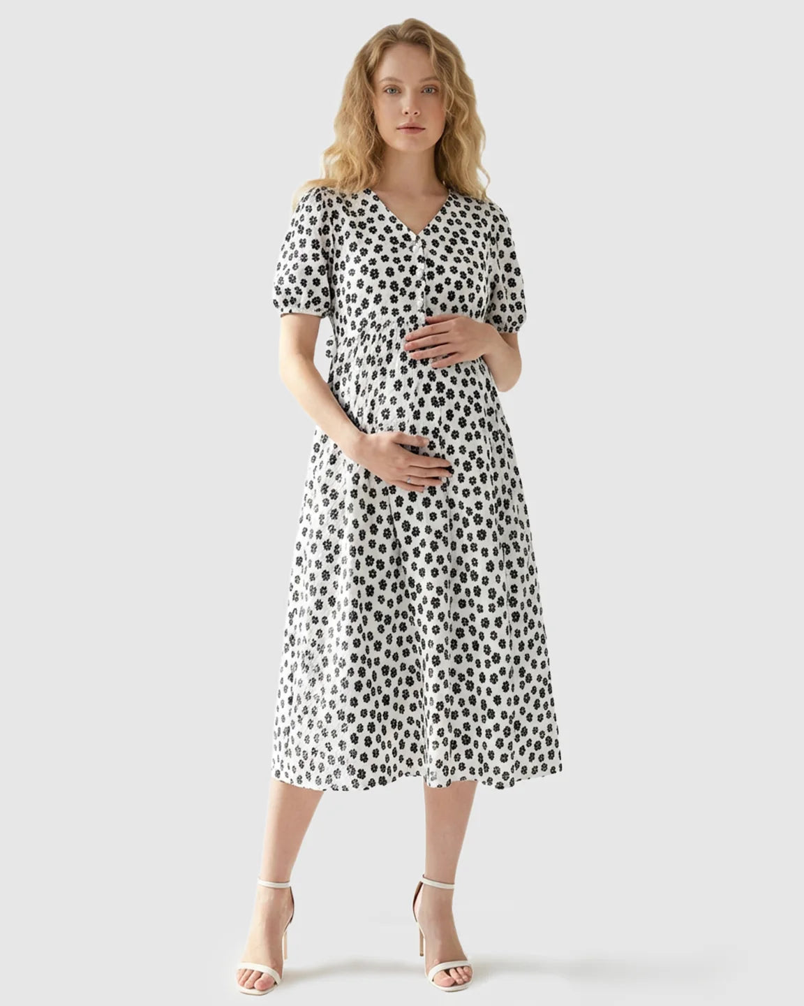Woman in a white midi maternity nursing dress with black floral print, V-neck, and button-front.