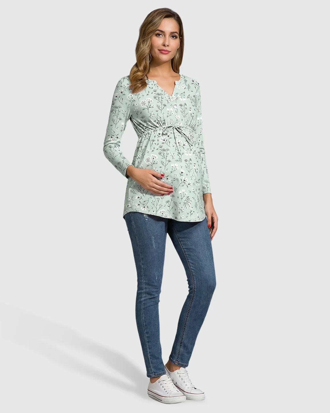 Pregnant woman in a light green floral long-sleeve maternity tunic with a notch neckline and drawstring waist.