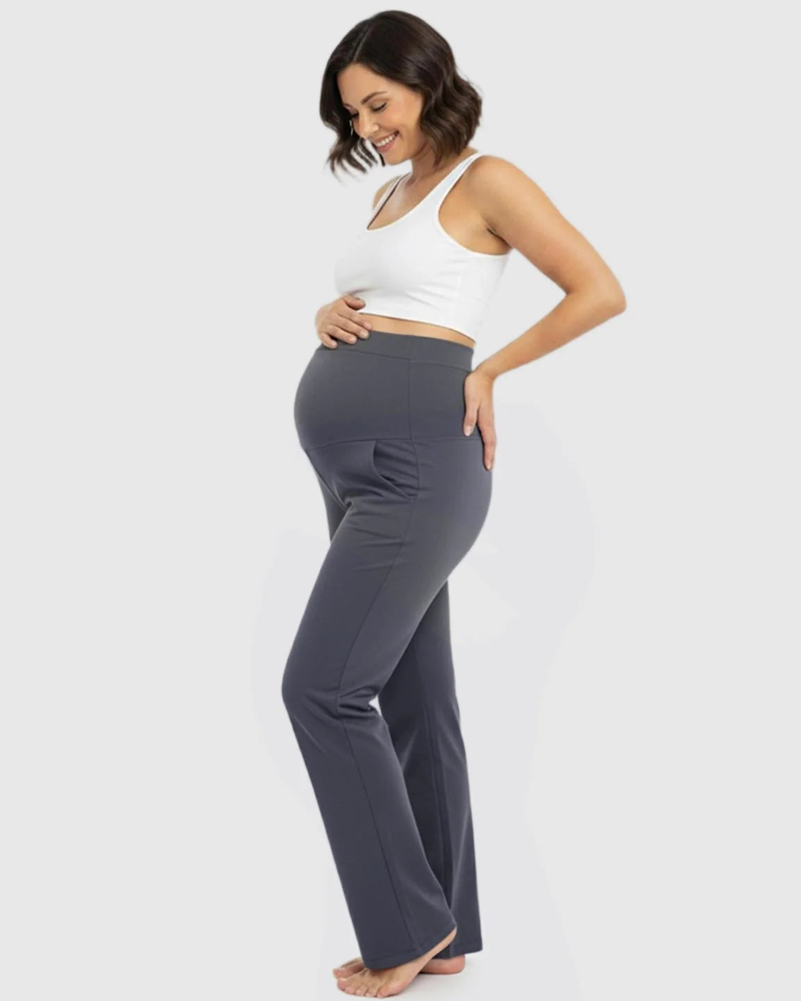 Smiling pregnant woman in charcoal gray stretch flared maternity pants with over-belly waistband and pockets.