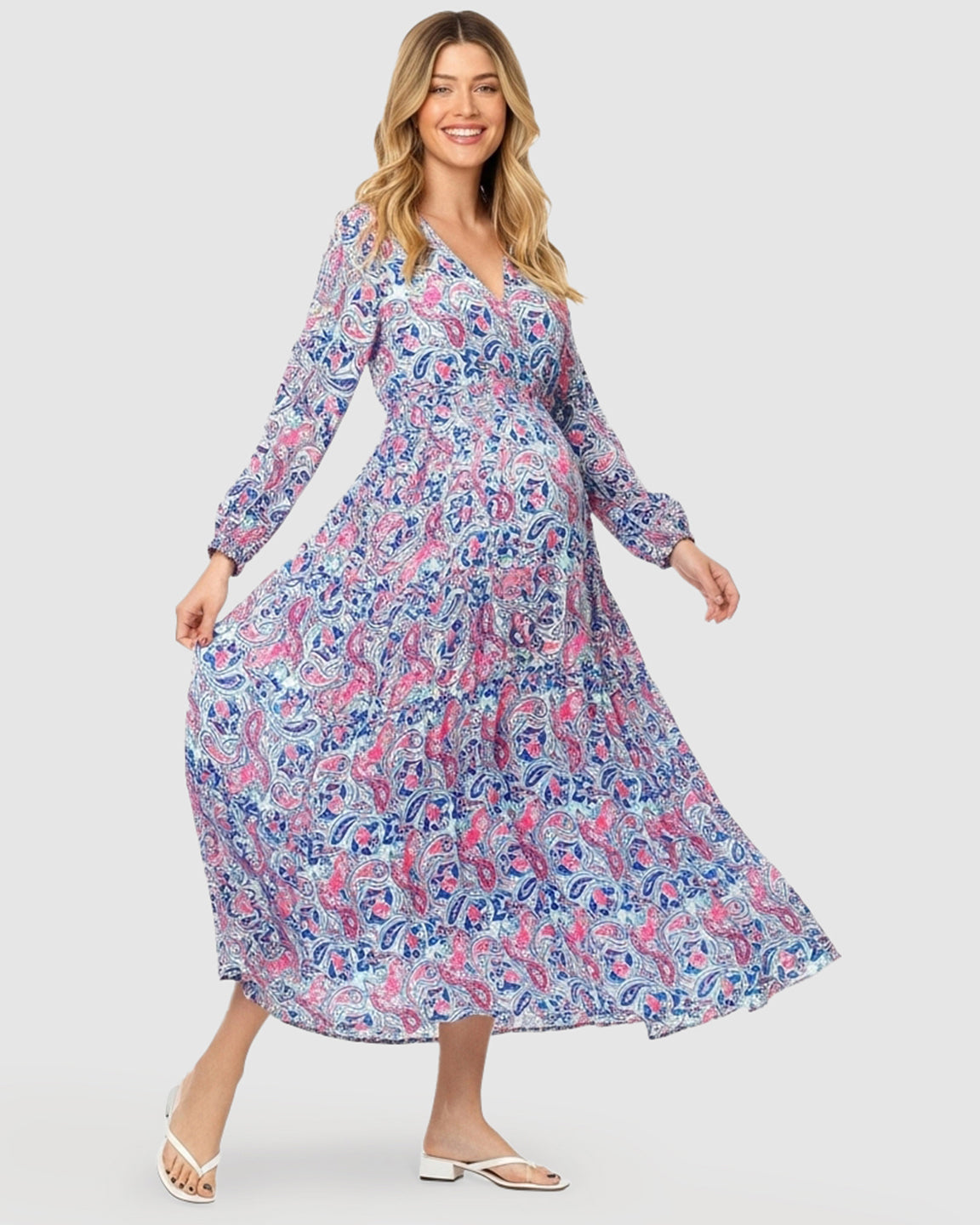 Smiling pregnant woman in a blue and pink paisley flowy maxi dress with long sleeves and a tie waist.