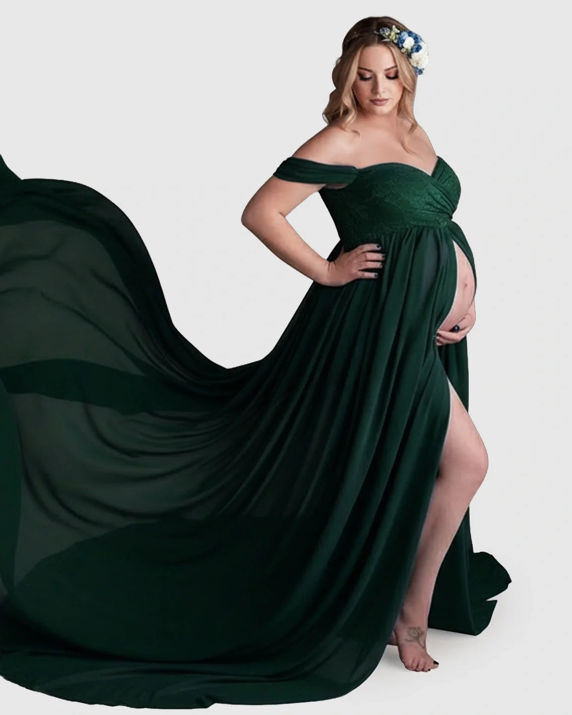 Pregnant woman in a dark green off-shoulder chiffon maternity gown with a long train and thigh-high slit.