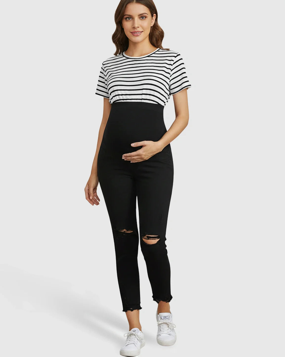 Pregnant woman in black ripped maternity skinny jeans with over-belly support panel and ankle-fray hem.
