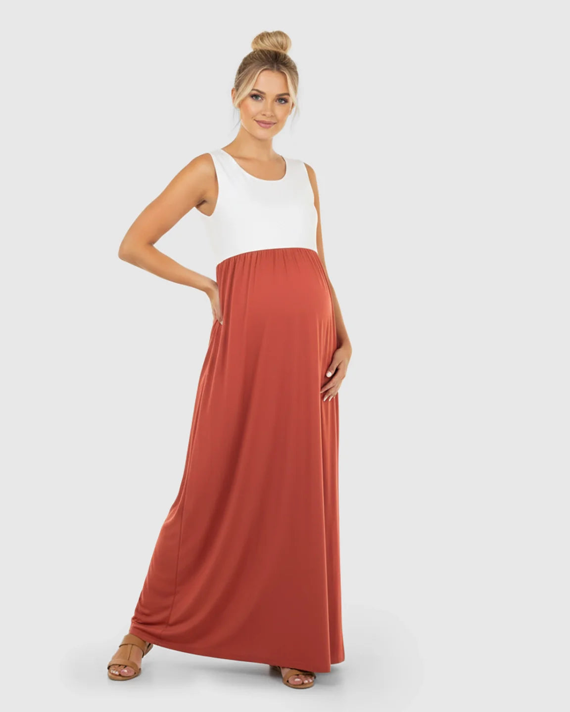 Smiling pregnant woman in a sleeveless, white and rust colorblock high-waisted maternity maxi dress.