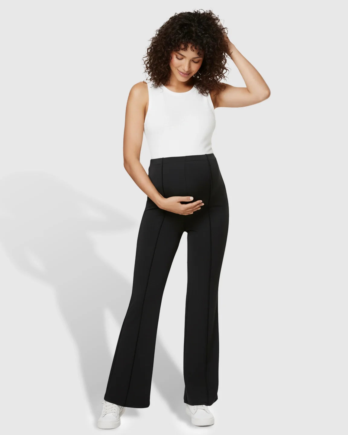 Pregnant woman in black butt-lifting flared maternity pants with an over-belly fit and white tank top.