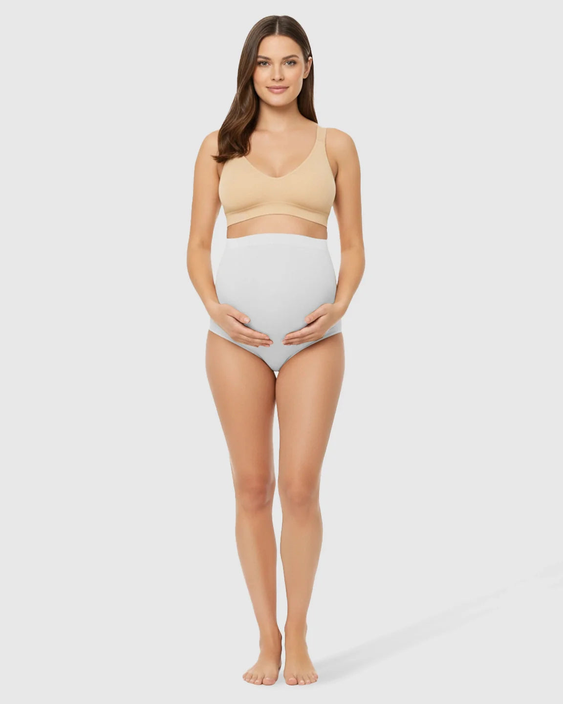 Smiling pregnant woman wearing a beige seamless maternity bra and light grey high-waist belly-support underwear.