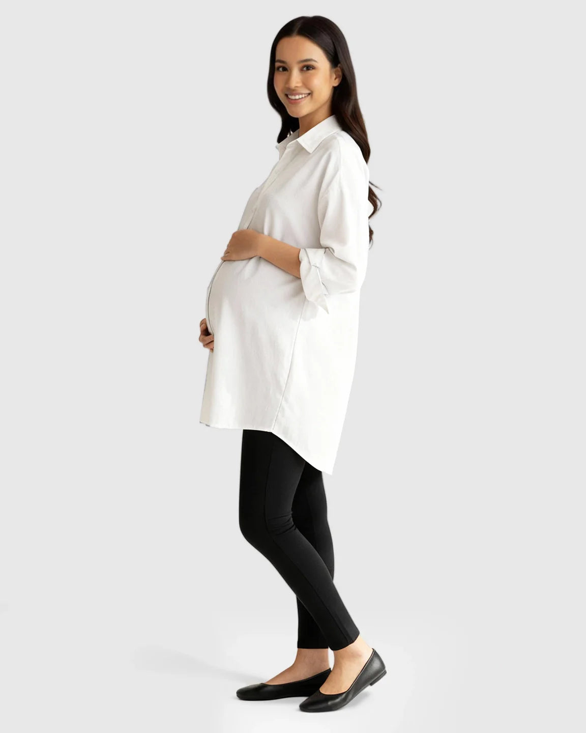 Smiling pregnant woman in a white cotton lapel-collar button-front maternity tunic and black leggings.