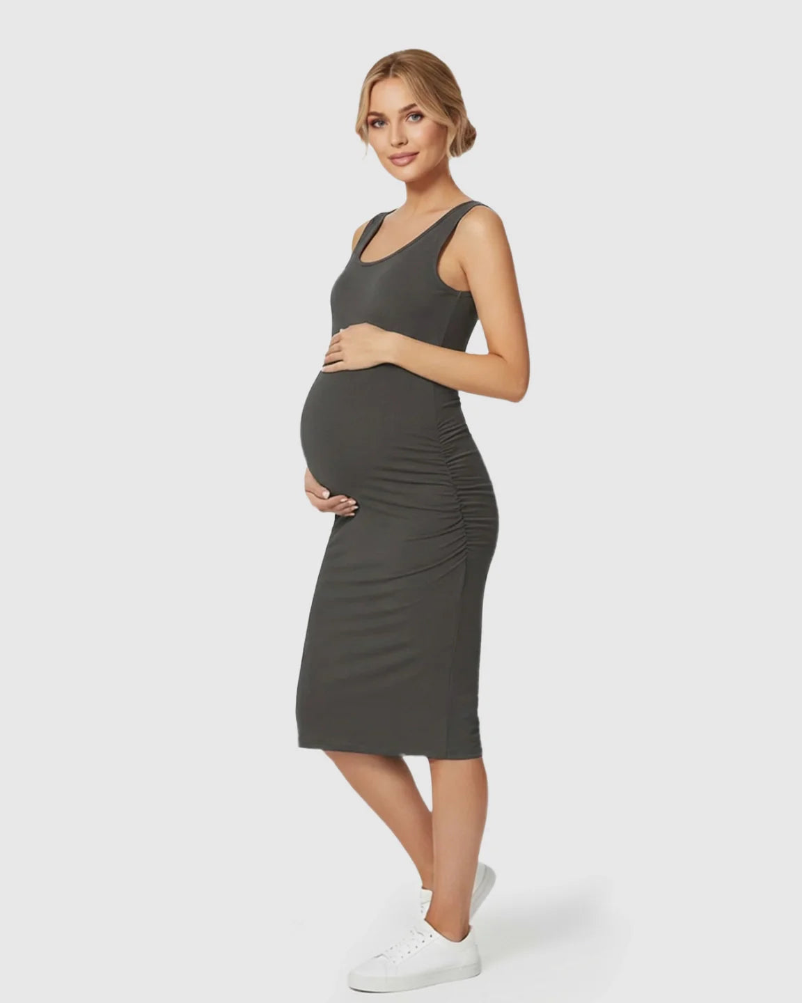 Pregnant woman in a charcoal sleeveless bodycon maternity dress with side ruching, paired with white sneakers.