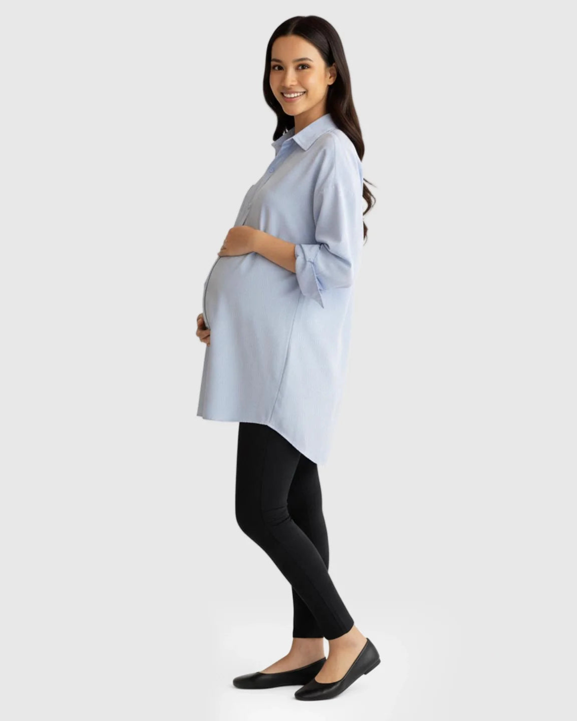 Smiling pregnant woman in a light blue cotton lapel-collar button-front maternity tunic and black leggings.