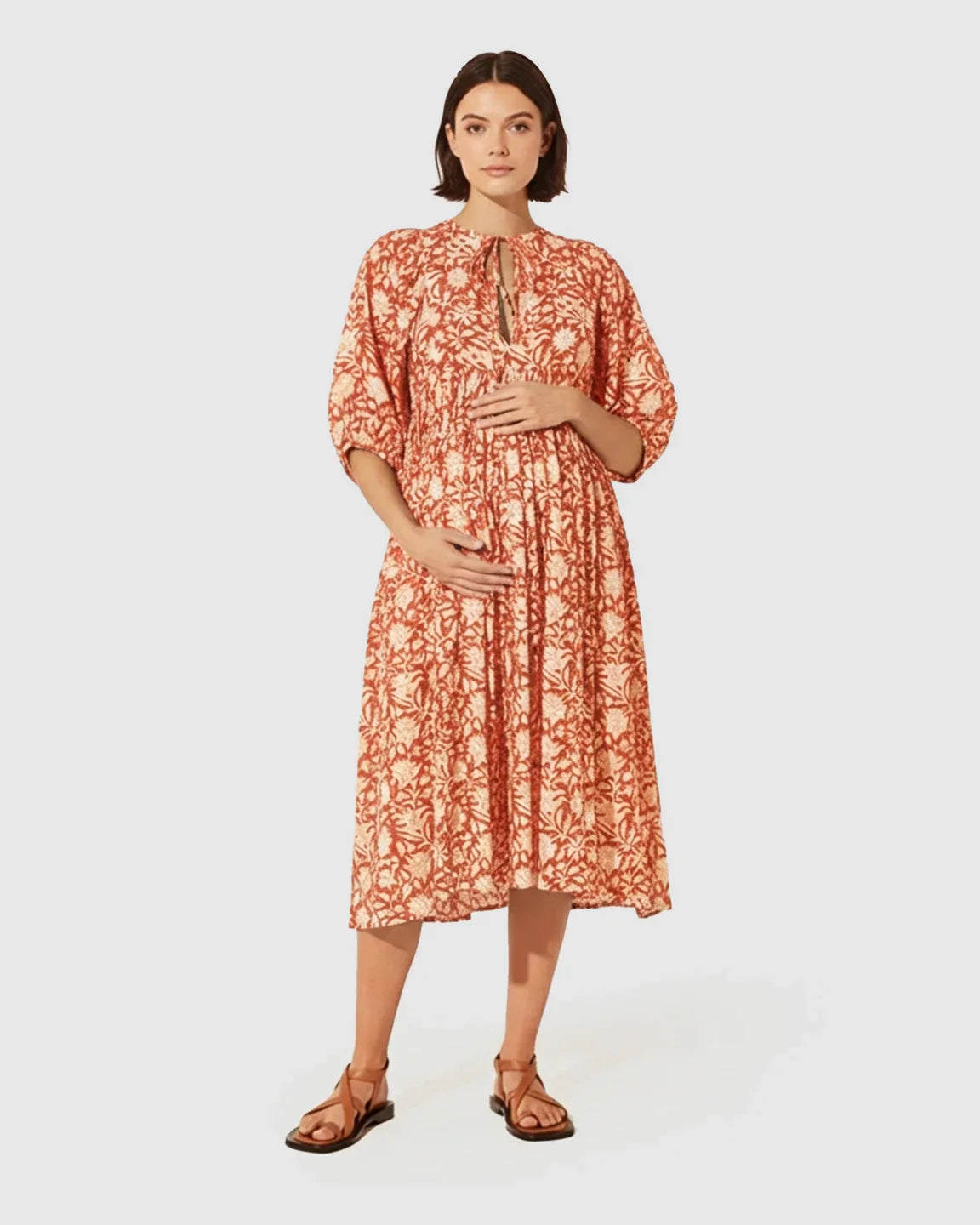 Pregnant woman in a terracotta floral maternity midi dress with gathered shoulders and puff sleeves.