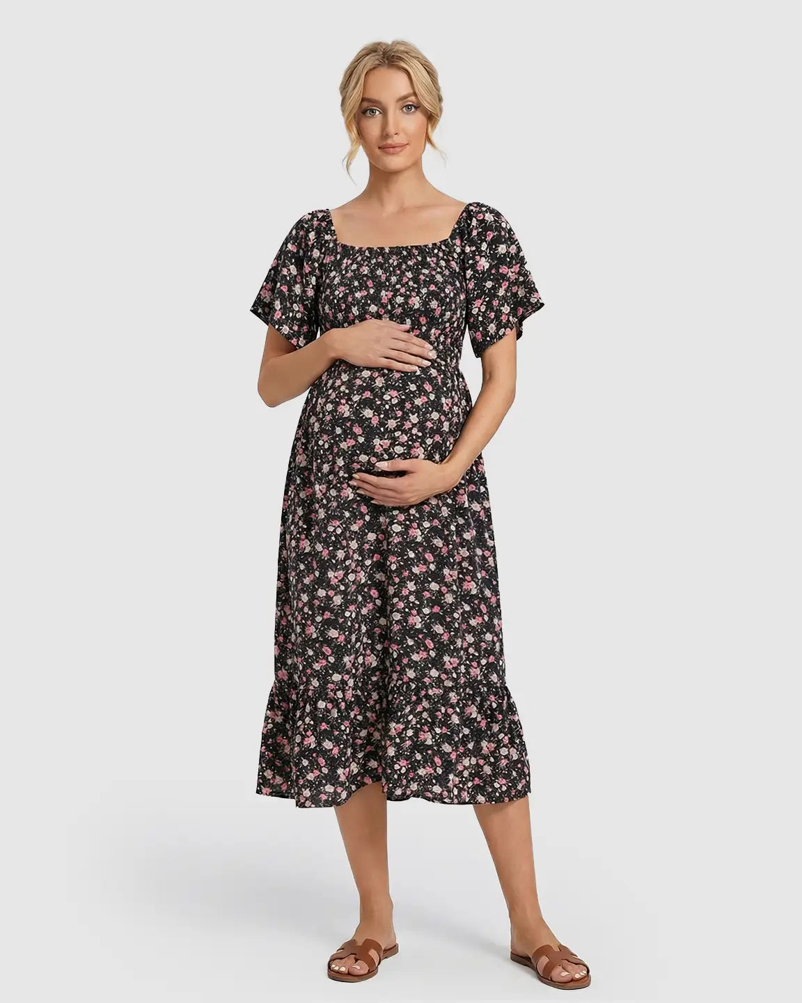 Pregnant woman in a black floral flutter-sleeve smocked maternity midi dress with pink flowers.