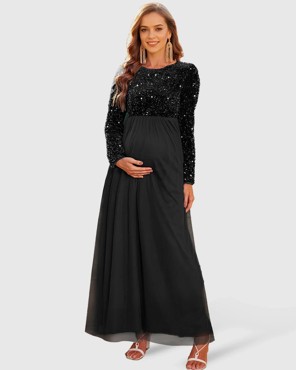 Smiling pregnant woman in a black sequin long-sleeve empire waist maternity maxi dress with mesh skirt.