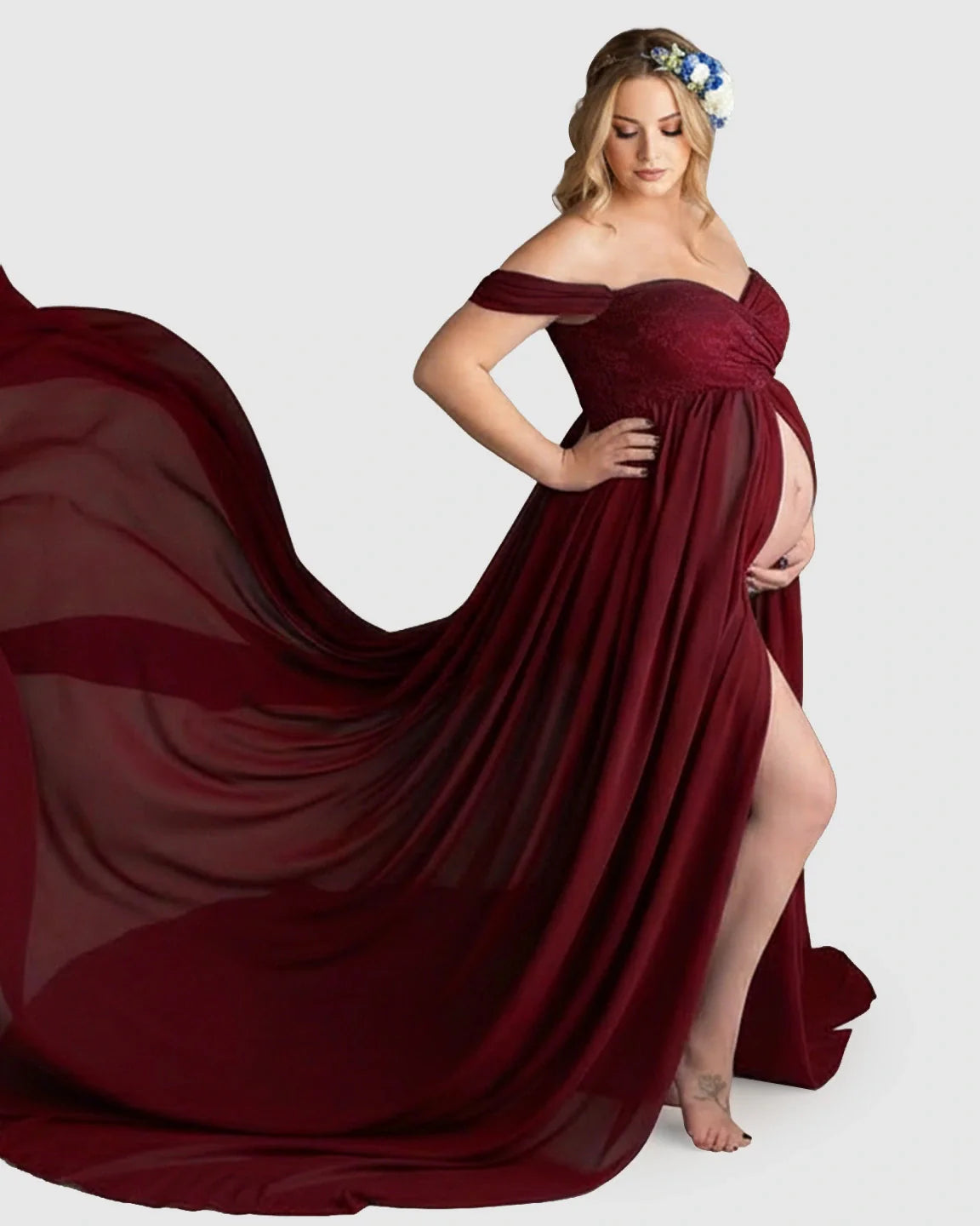 Pregnant woman in a flowing, off-shoulder burgundy chiffon maternity gown with a long train and thigh-high slit.