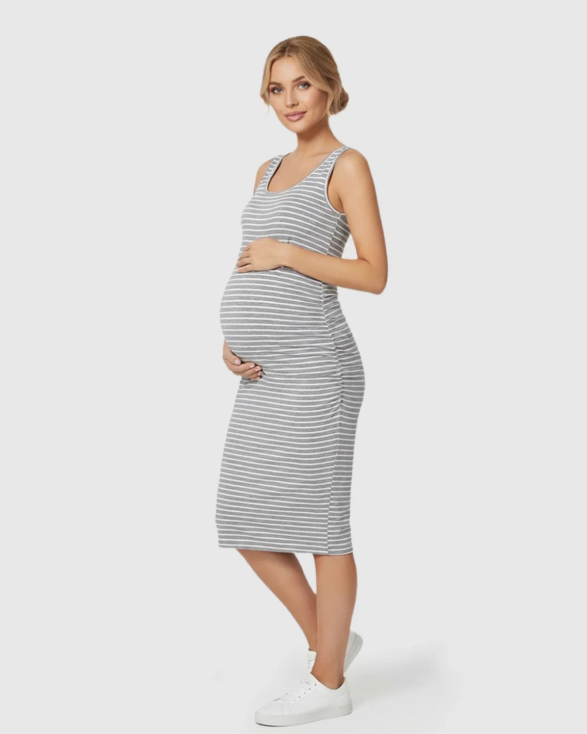 Pregnant woman in a grey and white striped sleeveless bodycon maternity dress, holding her belly.