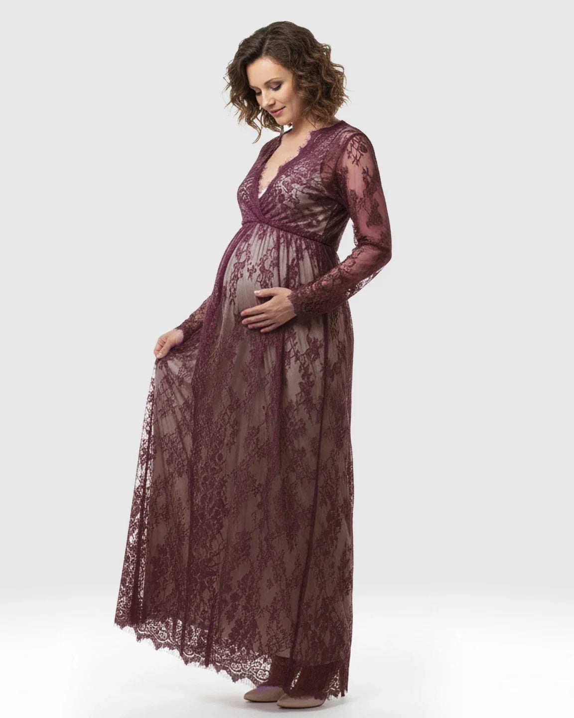 Maternity maxi dress in sheer floral plum lace with an empire waist and long sleeves, worn by a pregnant woman.