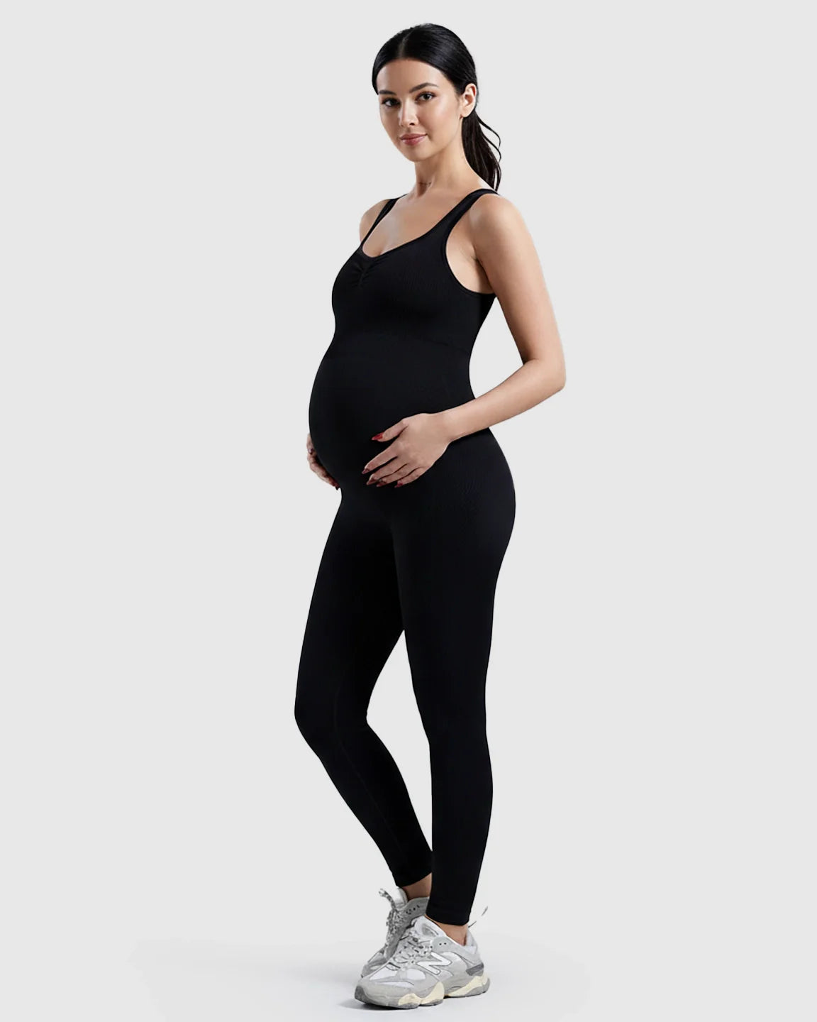 Black ribbed maternity bodysuit with scoop neck, high waist, and full-length legs, worn by a pregnant woman.