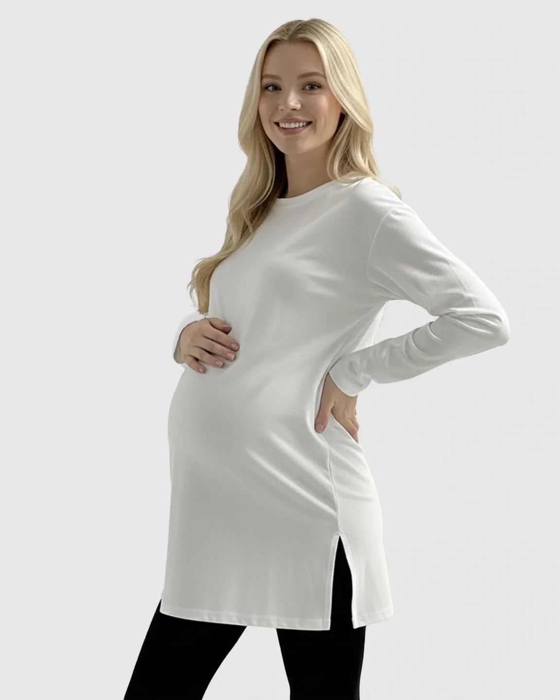 Smiling pregnant woman in a white long-sleeve cotton maternity top with side slits, paired with black leggings.
