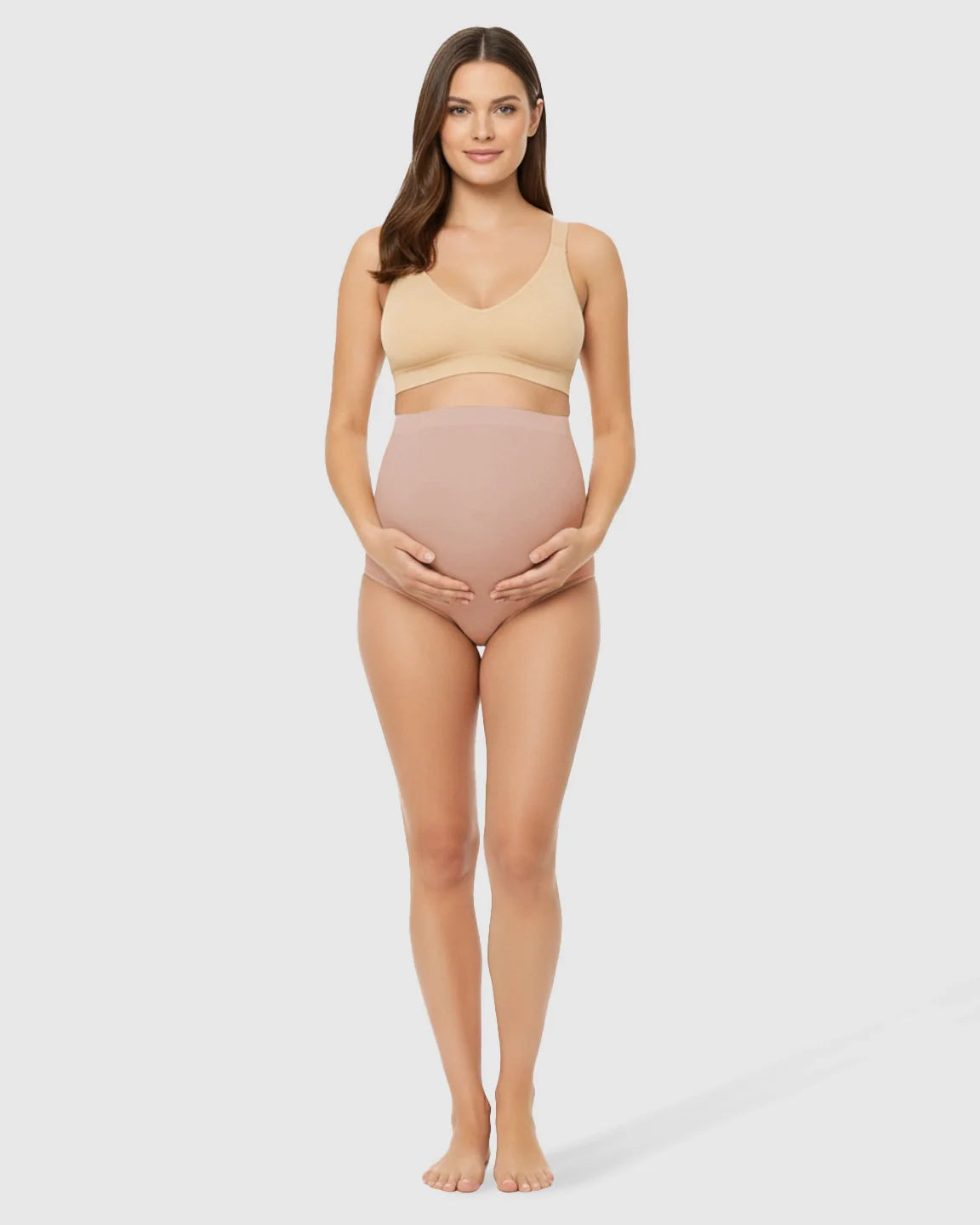Smiling pregnant woman in seamless nude high-waist belly-support maternity underwear and matching bra.