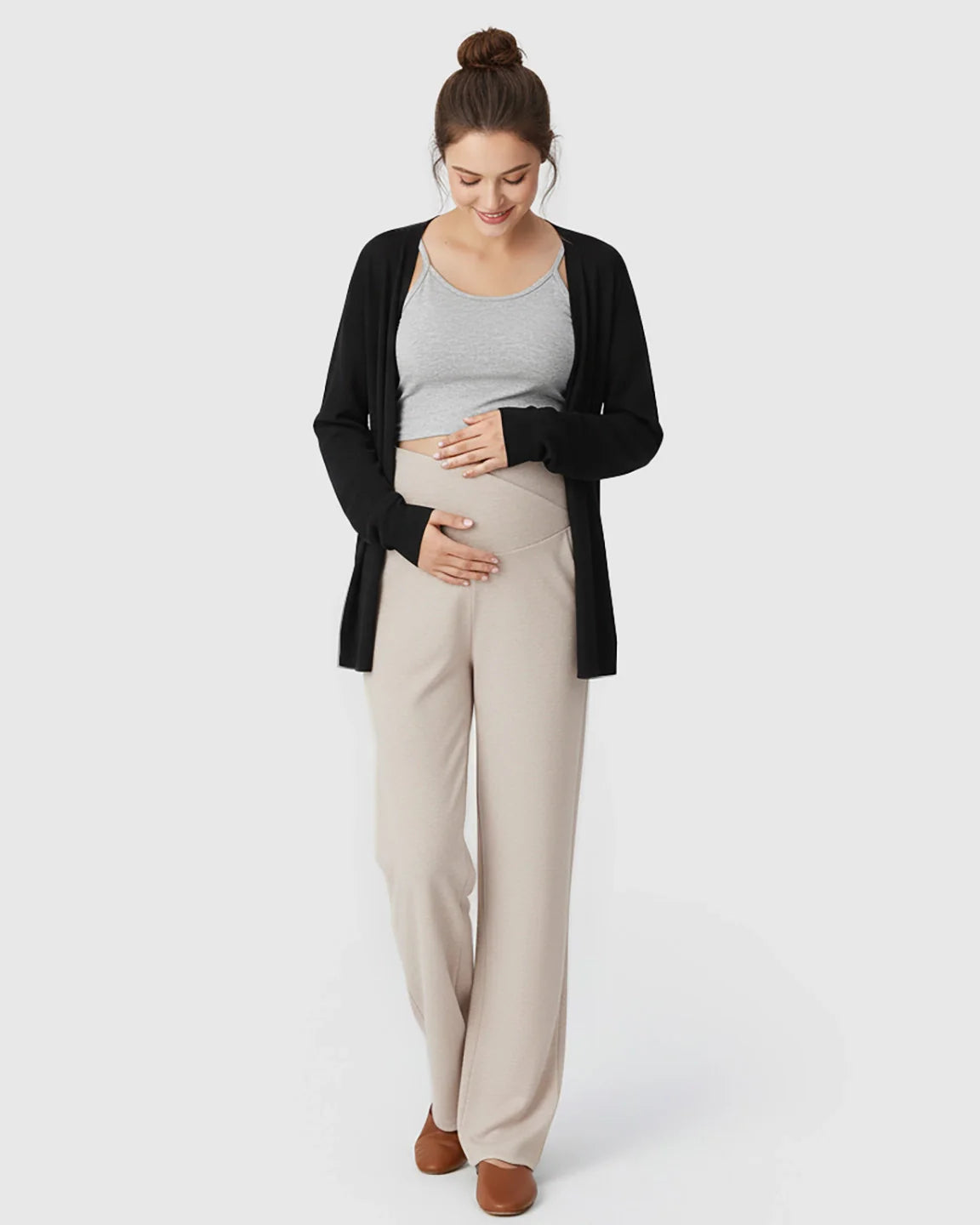Pregnant woman in beige crossover waist wide-leg maternity lounge pants, grey tank, and black cardigan.