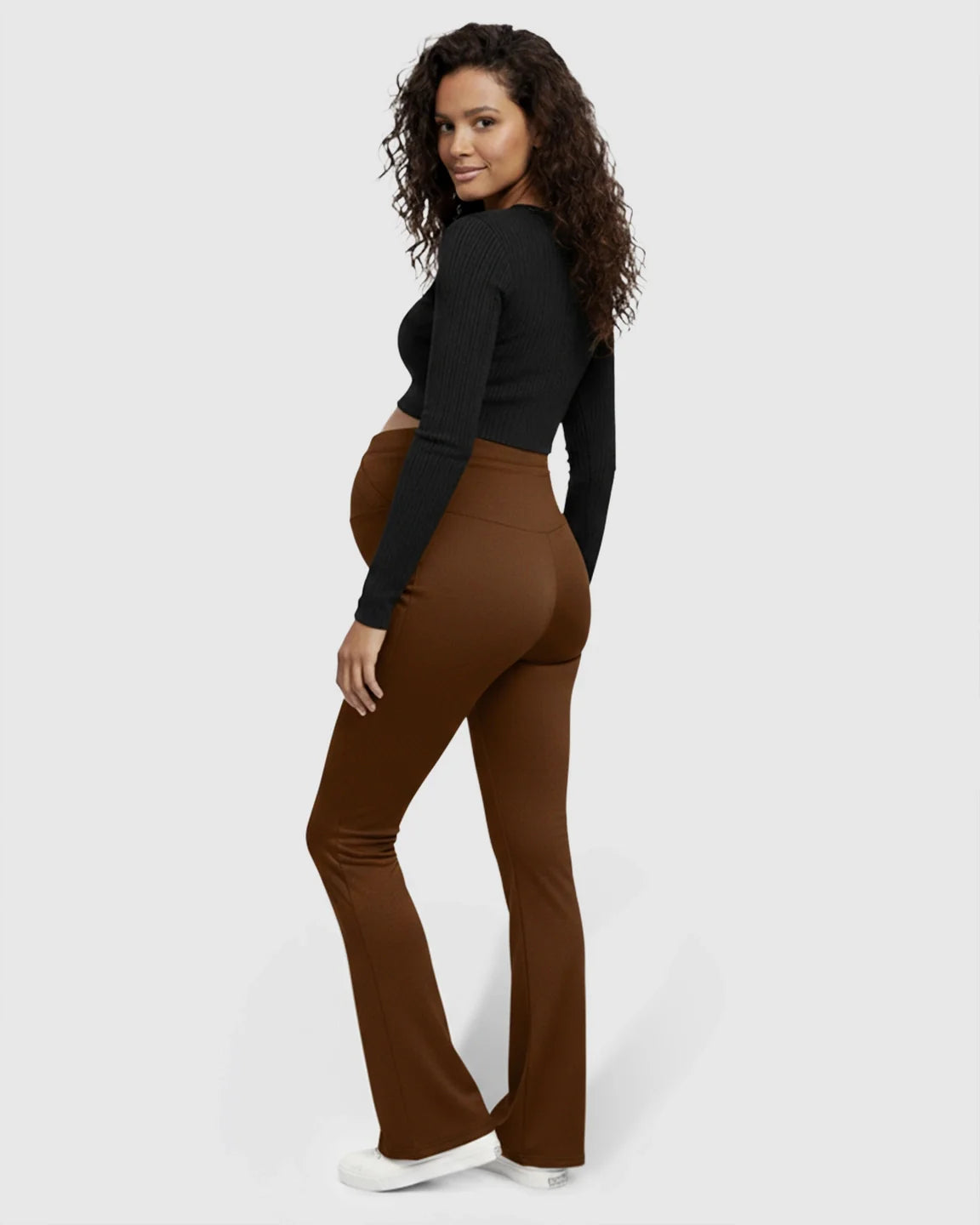 Pregnant woman in brown flared maternity pants with a crossed waistband and black long-sleeve top.