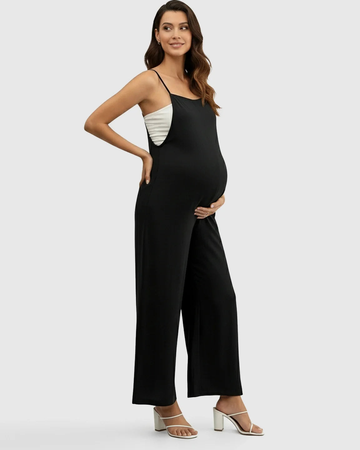 Pregnant woman in a black spaghetti strap wide-leg maternity jumpsuit with a white top underneath.