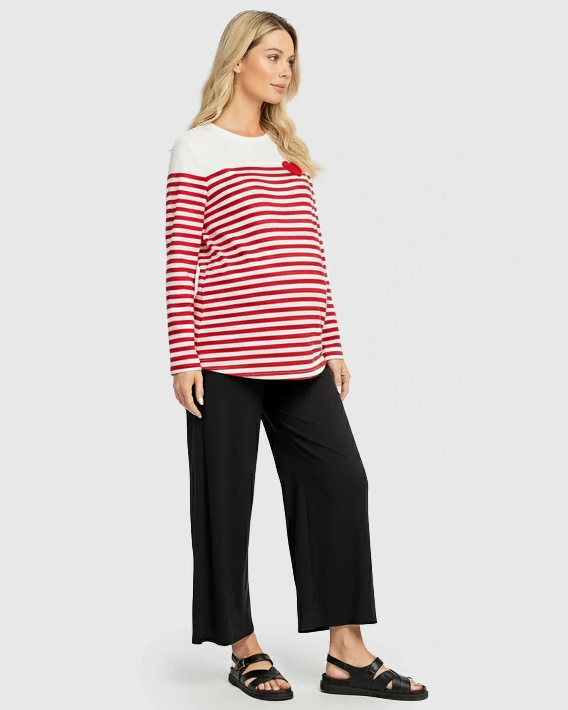 Blonde pregnant woman wearing a red and white striped long-sleeve maternity top with a red heart detail.