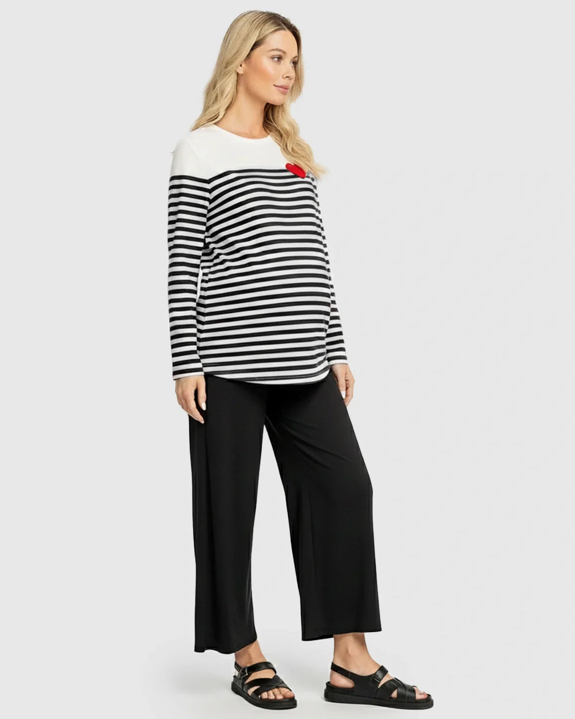Blonde pregnant woman in a black and white striped long-sleeve maternity top with a red heart and black pants.