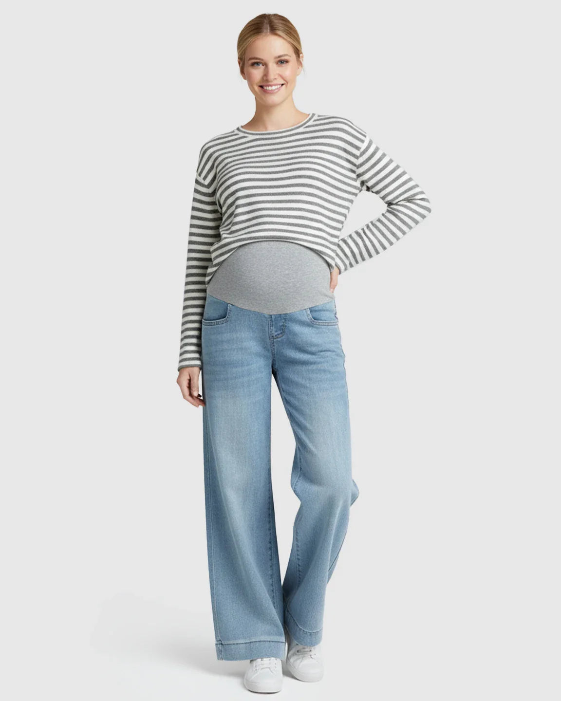 Smiling pregnant woman in light wash wide leg maternity jeans with a folded hem and grey belly band.