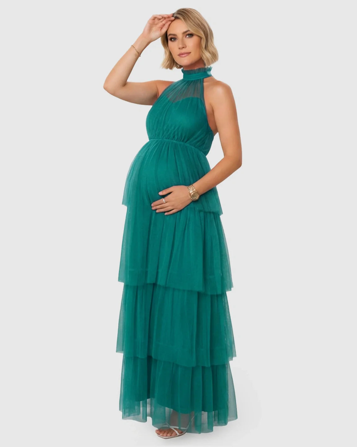 Pregnant woman in a teal halter neck tiered mesh maternity gown, holding her bump.