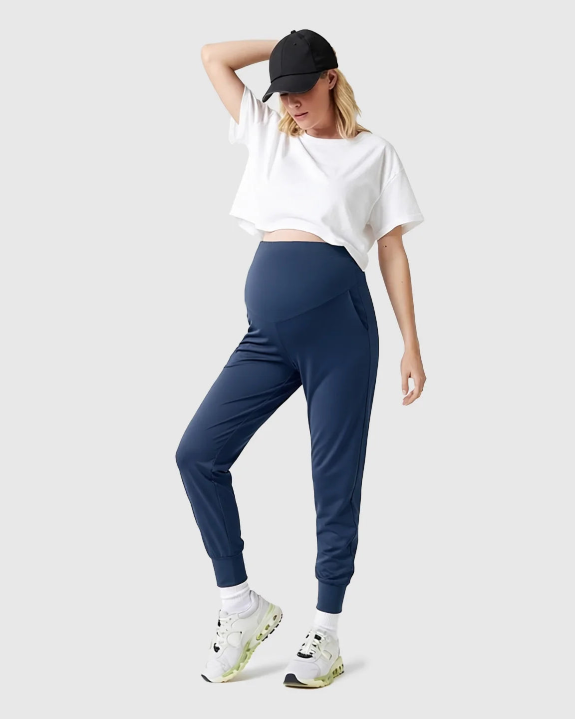 Pregnant woman wearing navy supportive slim-fitting maternity joggers with a high-waist design and white crop top.