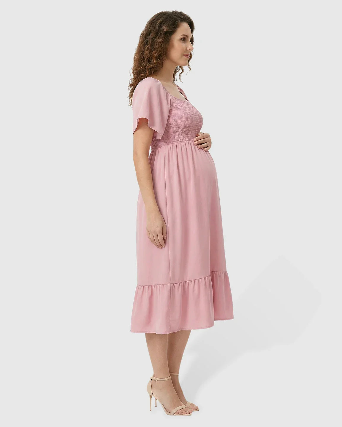Pink flutter-sleeve smocked maternity midi dress with a tiered skirt, worn by a pregnant woman.
