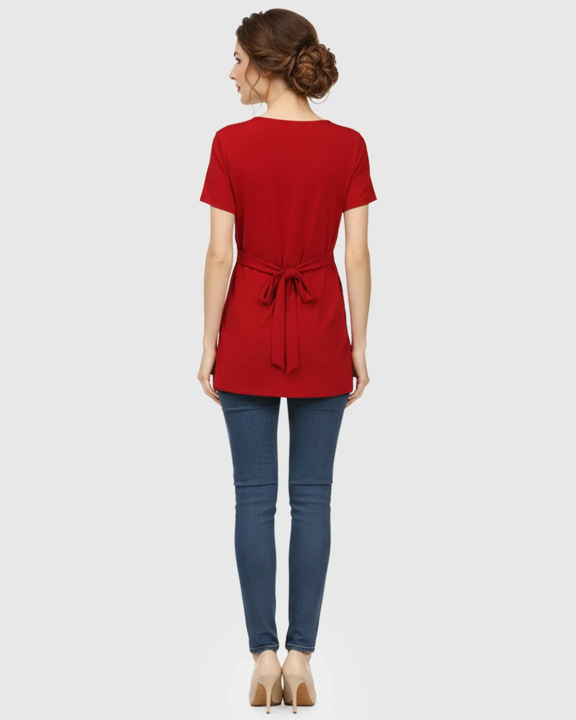 Woman from behind wearing a red V-neck wrap-style maternity top with a tied waist, blue jeans, and heels.