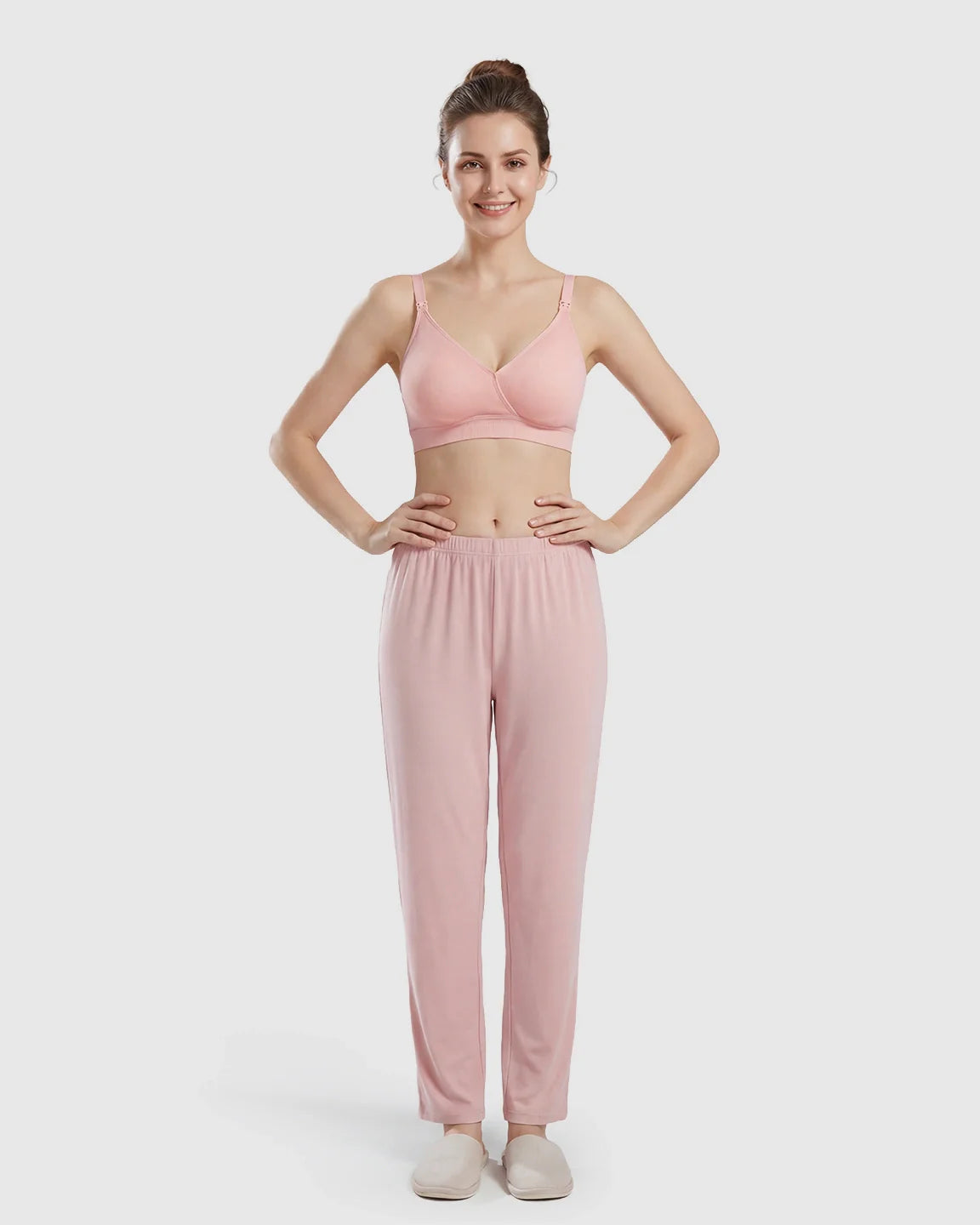 Smiling woman models a pink seamless cross-front wireless nursing bra and matching lounge pants.
