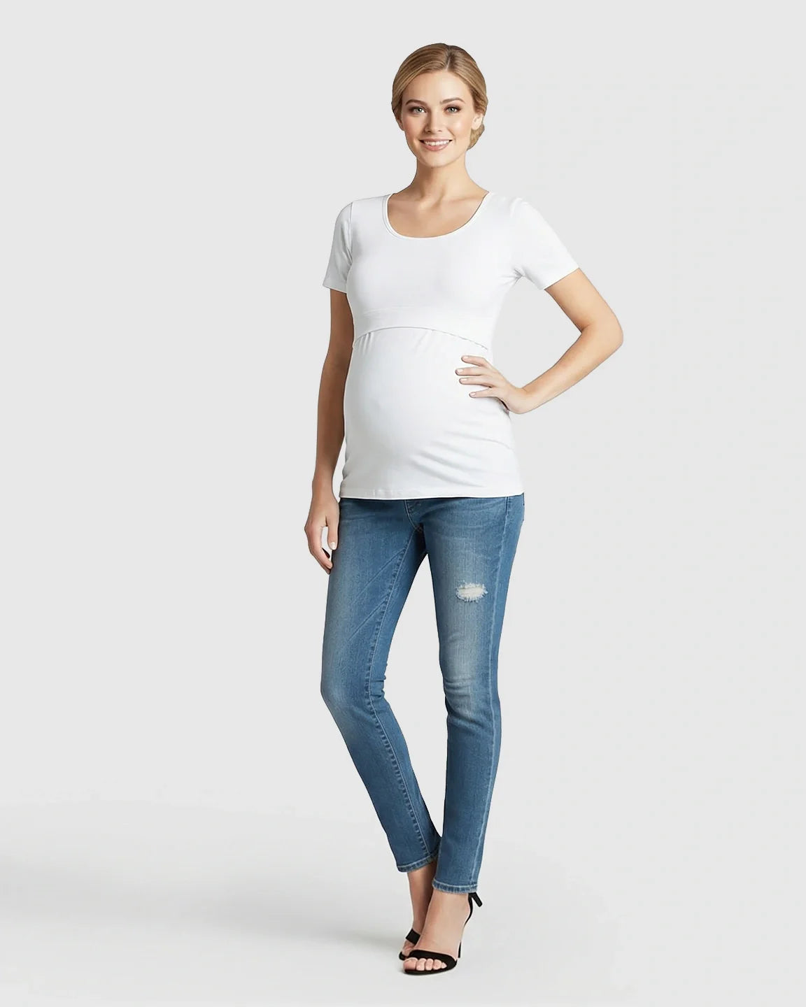 Smiling pregnant woman in a white stretch-fit V-neck nursing t-shirt and blue jeans.