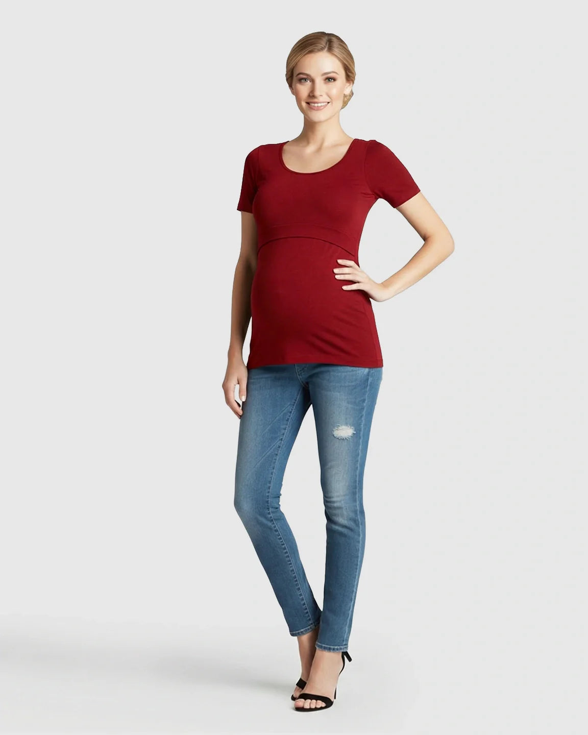 Smiling pregnant woman in a red stretch-fit scoop-neck nursing t-shirt and blue jeans.