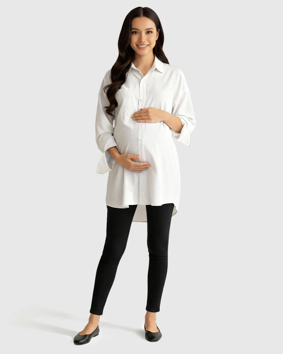 Smiling pregnant woman in a white cotton lapel-collar button-front maternity tunic and black leggings.