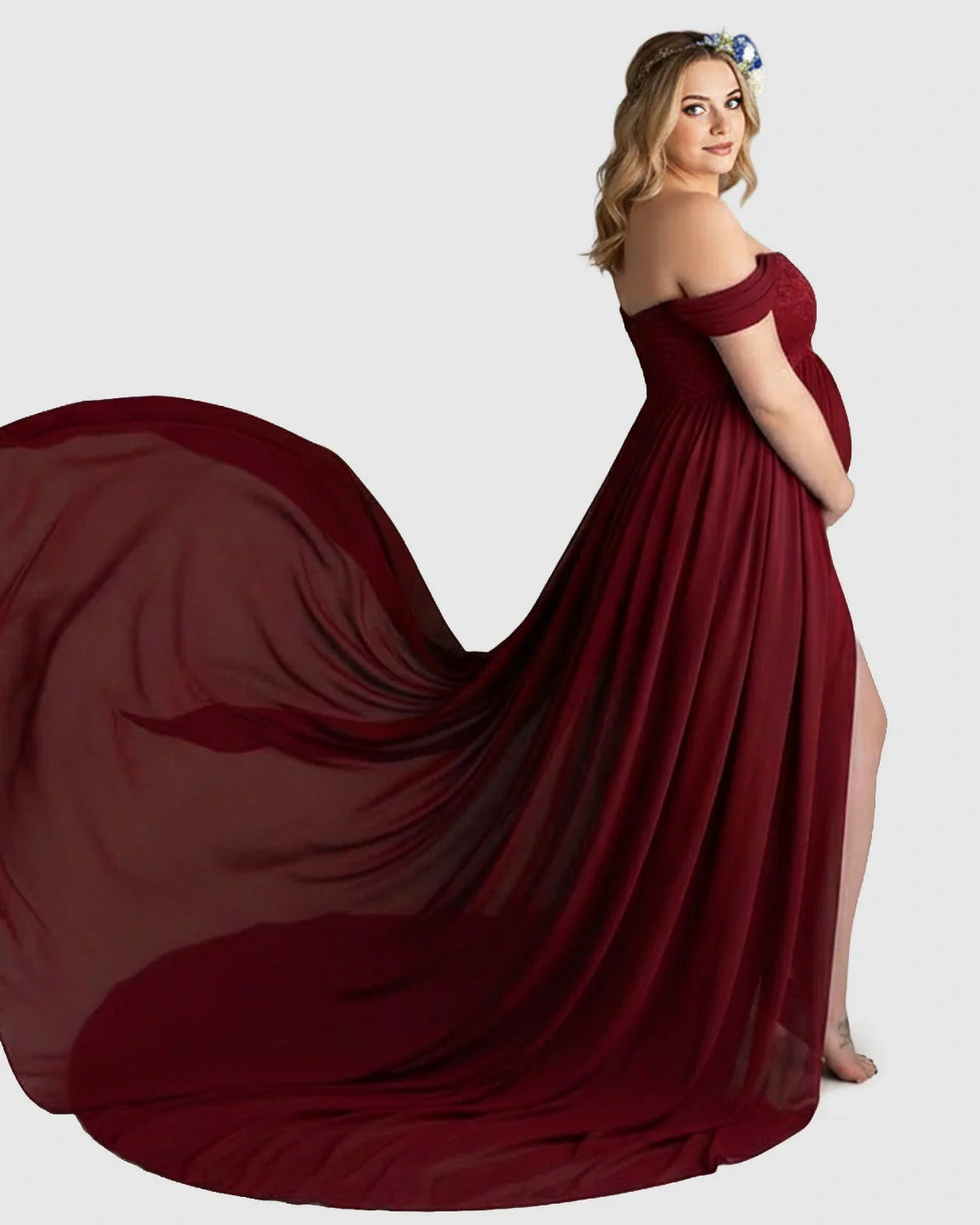 Pregnant woman in a flowing, off-shoulder maroon chiffon maternity gown with a long train and thigh-high slit.