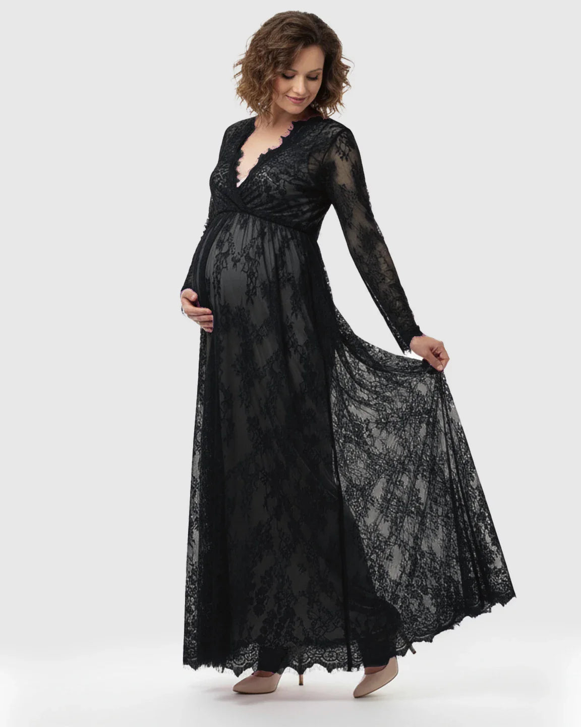 Pregnant woman in a black sheer floral lace empire waist maternity maxi dress, holding her bump and skirt.