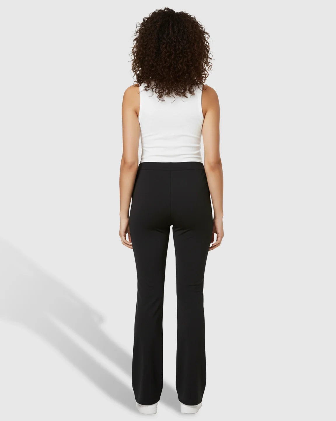 Woman from behind wearing black butt-lifting flared maternity pants and a white tank top.