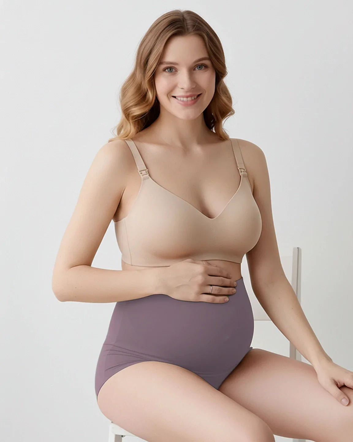 Smiling pregnant woman wearing a nude maternity bra and high-waist, seamless purple maternity briefs.