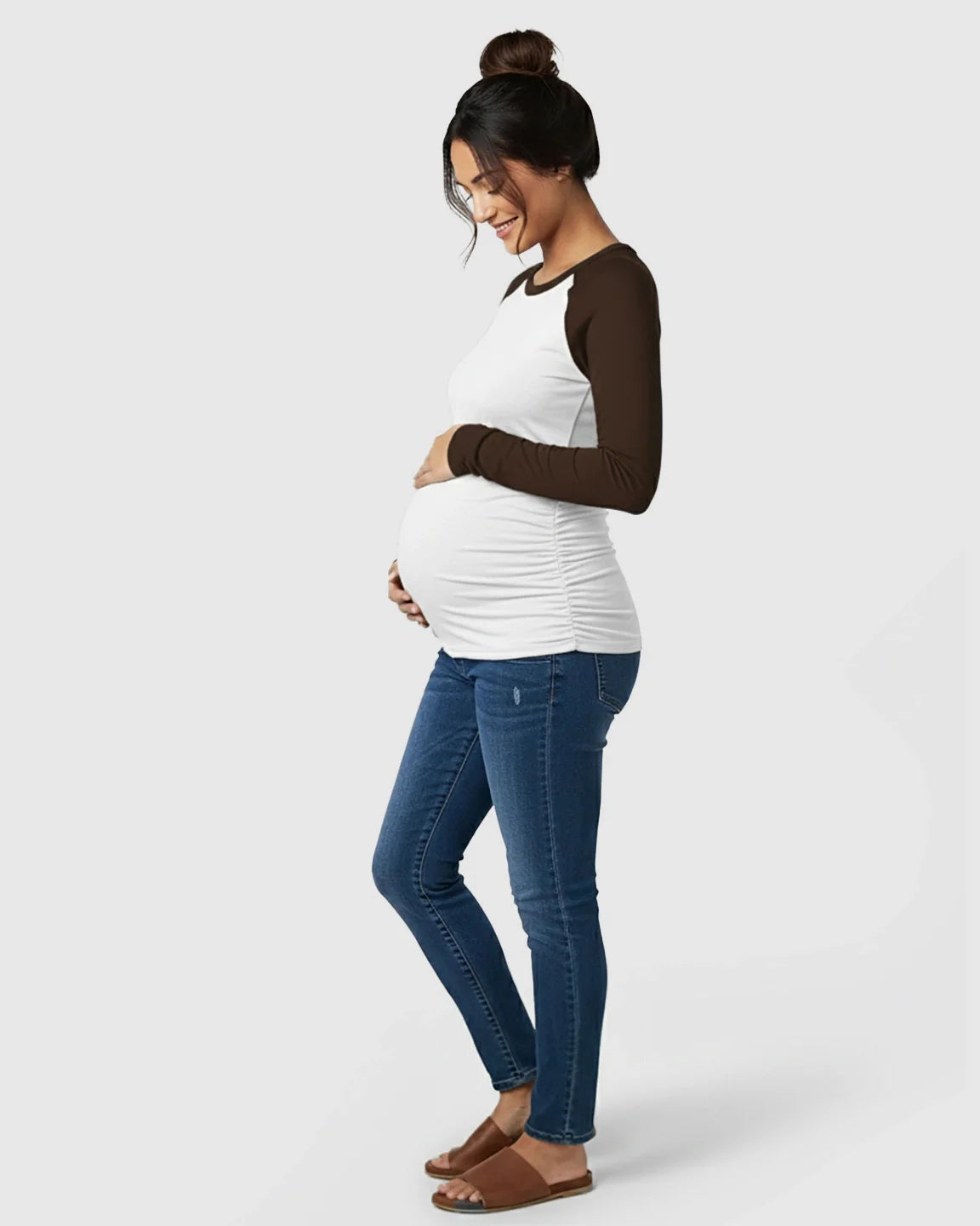 Pregnant woman in a white and brown raglan long-sleeve maternity top with ruched sides and blue jeans.